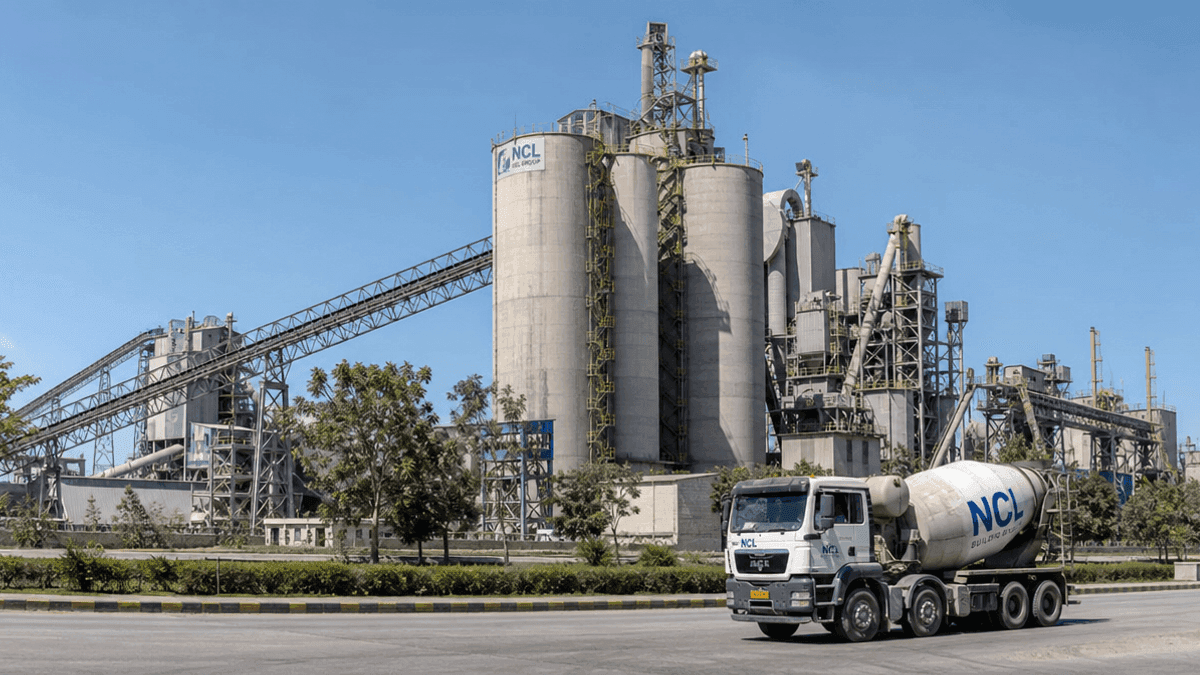 A view of a cement manufacturing plant with silos and industrial machinery under a clear sky.